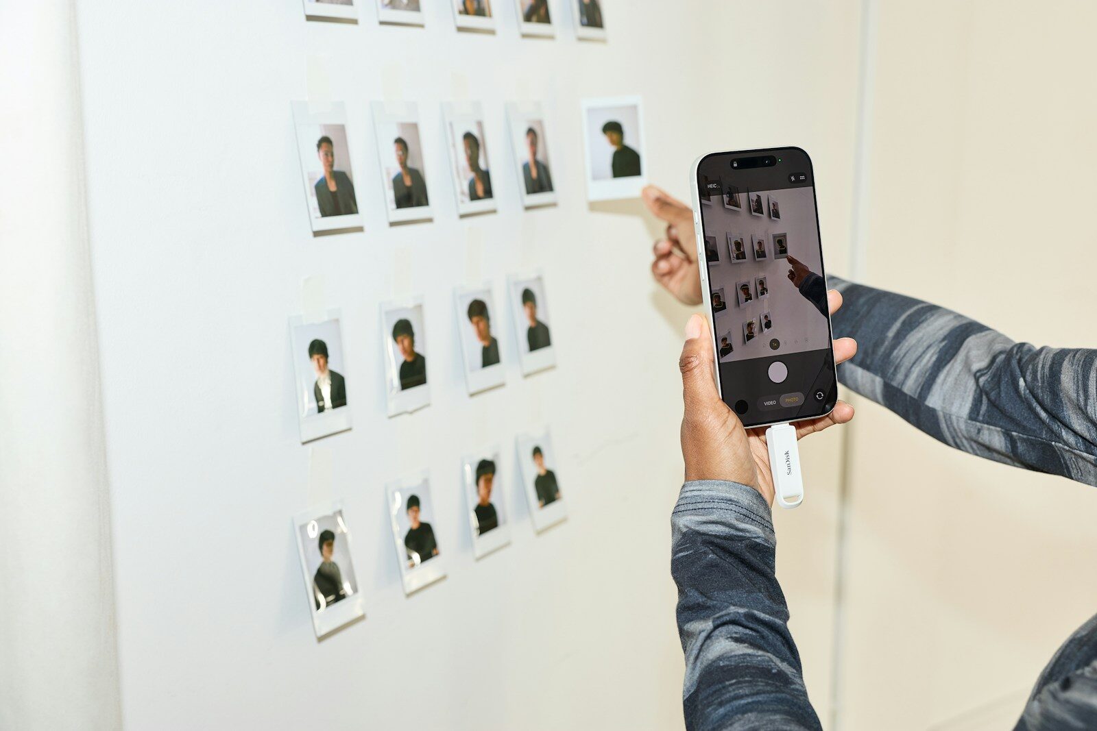 Person photographs small pictures on a white wall with phone